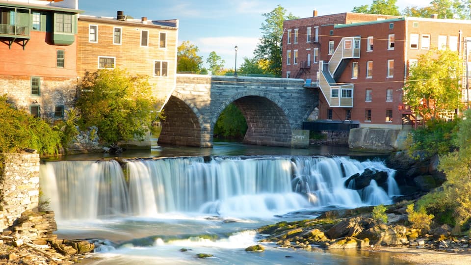 A stone bridge over a flowing river, surrounded by buildings and greenery.