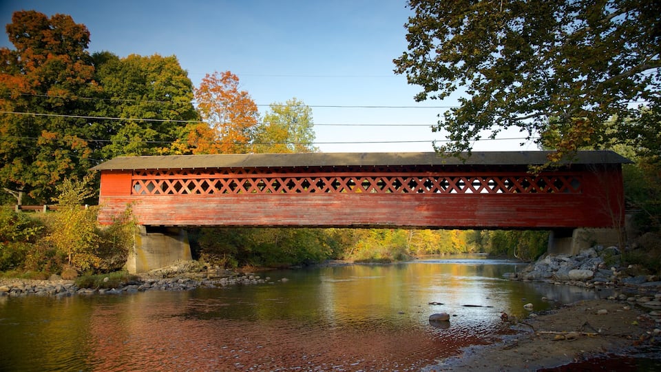 A red covered bridge over a river with autumn foliage.