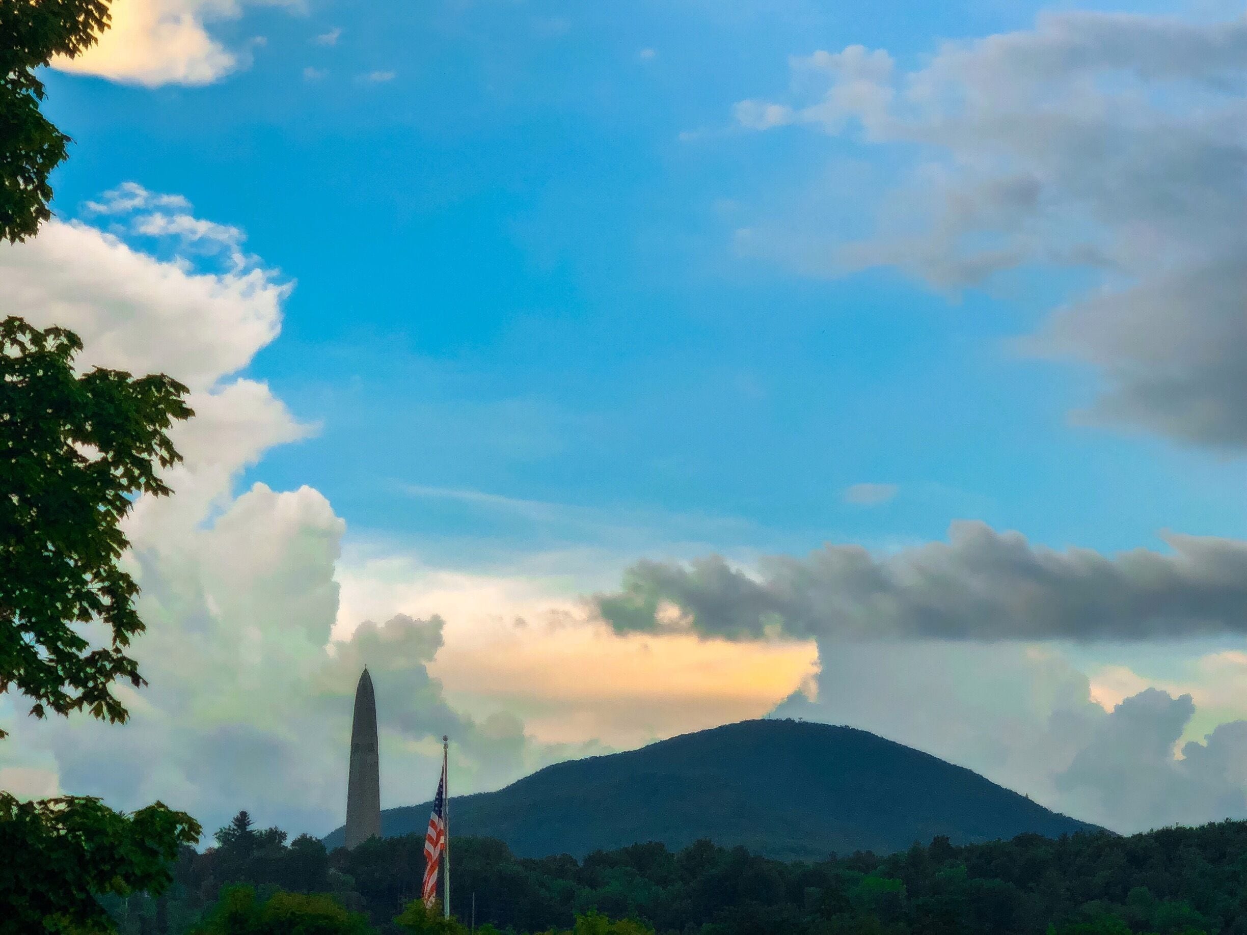 A mountain with a flag, a tall monument, and a partly cloudy sky.