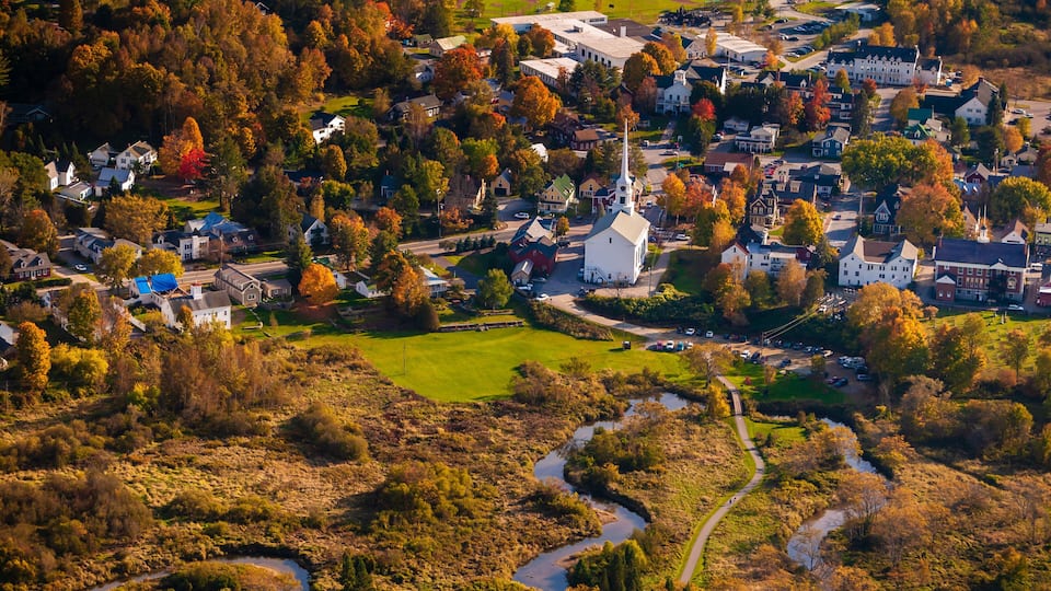 An aerial view of a town with a prominent church, winding roads, and autumn-colored trees.