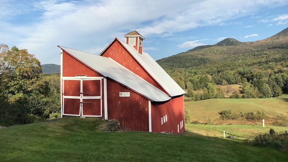 A red barn with a white roof and a chimney, surrounded by green fields and hills.