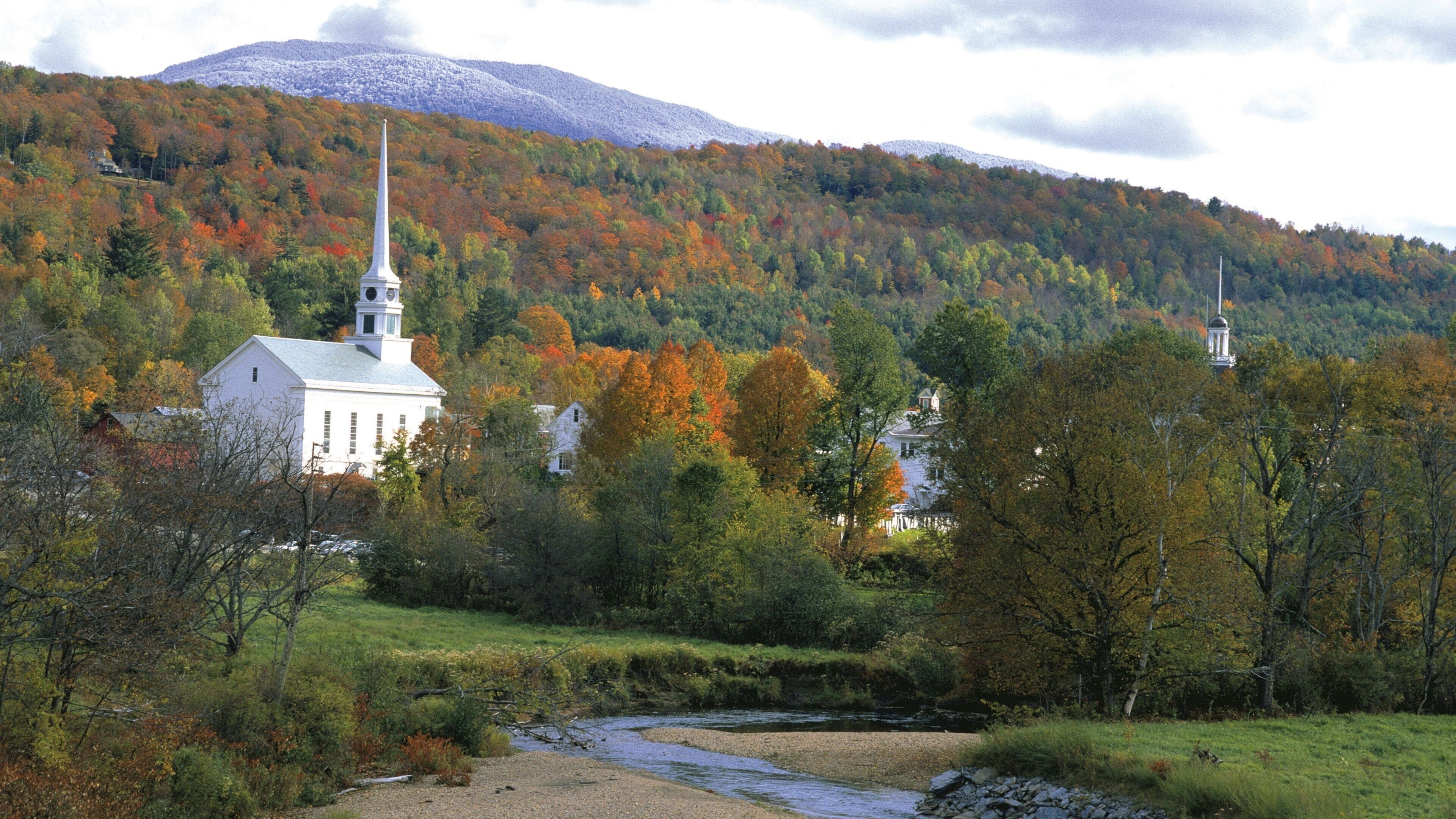 A church surrounded by autumn foliage and a mountain in the background.
