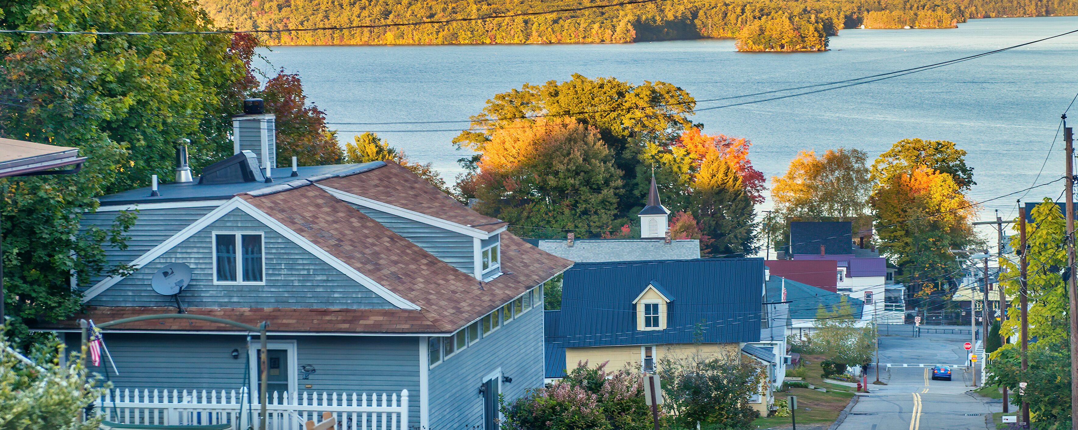 A residential area with houses, a white picket fence, and a lake in the background.