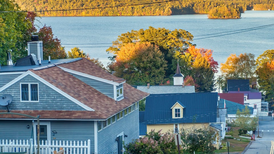 A residential area with houses, a white picket fence, and a lake in the background.