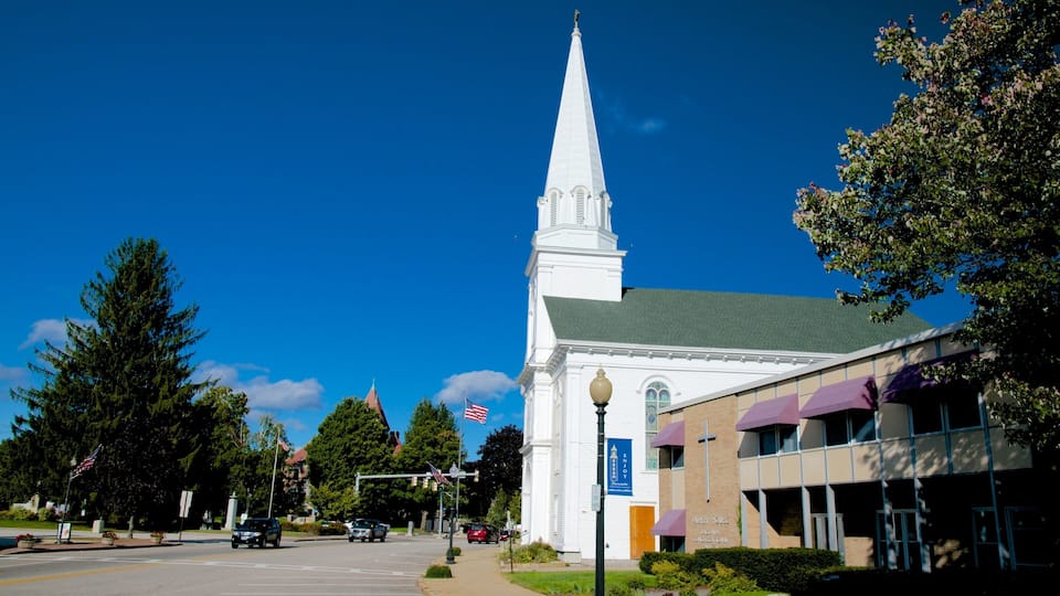 A church with a tall steeple, a parking lot, and a building with a sign that reads "ENJOY".