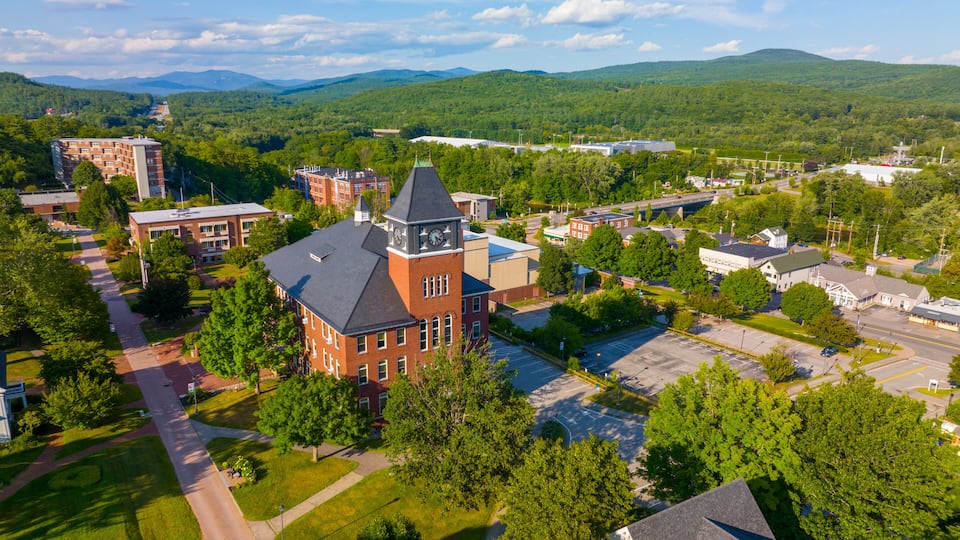 An aerial view of a campus with a prominent clock tower, surrounded by lush green hills and a clear sky.