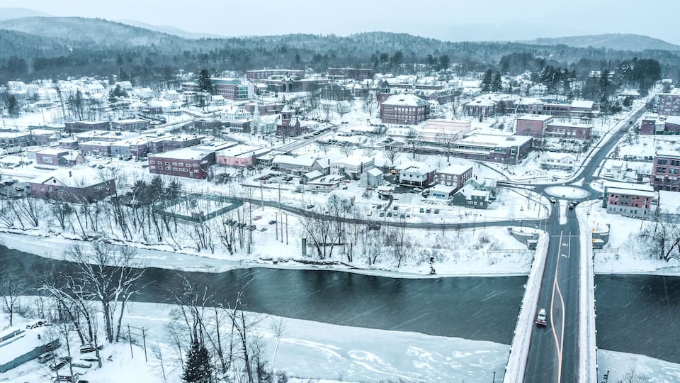 A snow-covered town with a river, buildings, and a bridge.