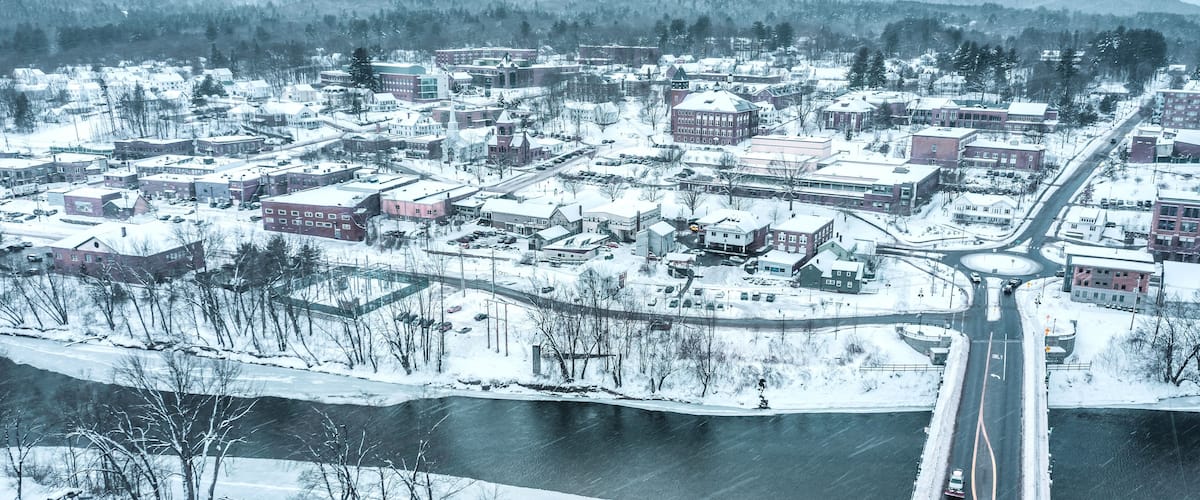 A snow-covered town with a river, buildings, and a bridge.