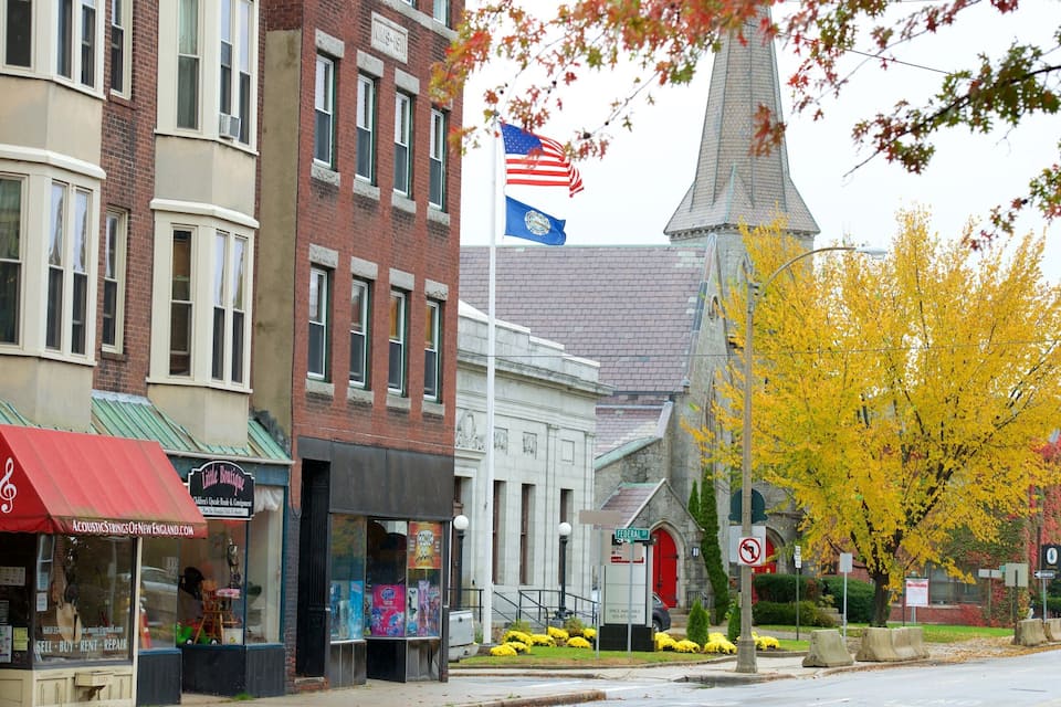 A street with historic buildings, a church steeple, and autumn foliage.