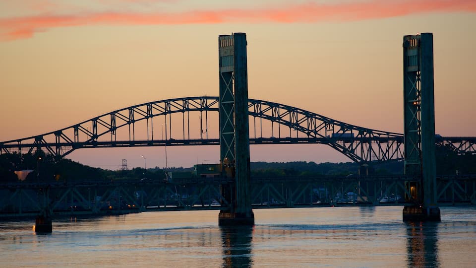 A bridge with two large towers over a body of water during sunset.