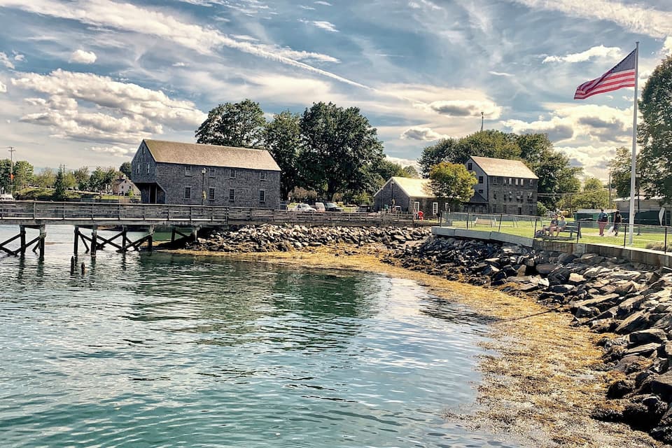 A waterfront with stone buildings, a wooden bridge, and an American flag.