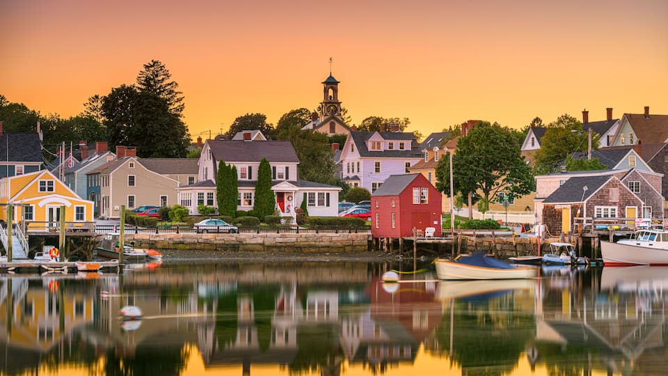 A harbor with boats, a church with a steeple, and colorful houses reflecting on the water.