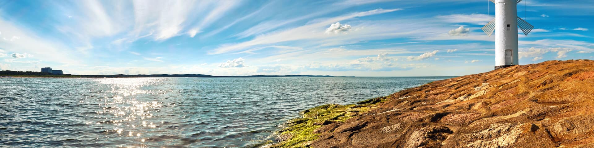 A lighthouse on a rocky shore with a clear sky and calm sea.