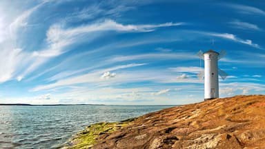 Un faro sobre una costa rocosa, con cielo despejado y mar tranquilo.