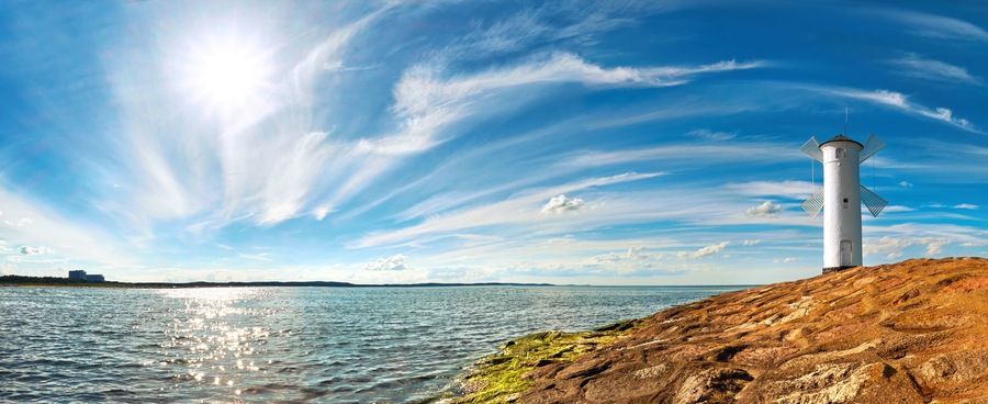 A lighthouse on a rocky shore with a clear sky and calm sea.