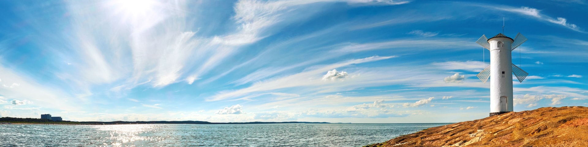 A lighthouse on a rocky shore with a clear sky and calm sea.