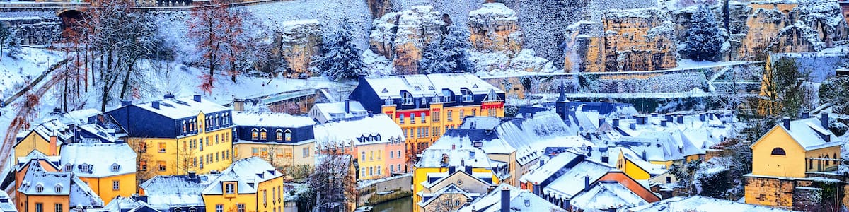 A snow-covered town with historic buildings, a river, and a bridge.