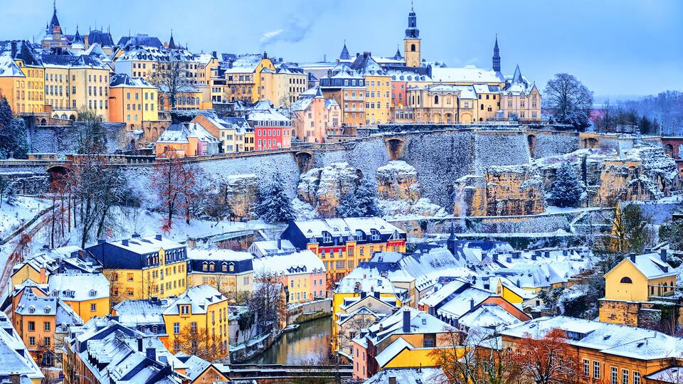 A snow-covered town with historic buildings, a river, and a bridge.