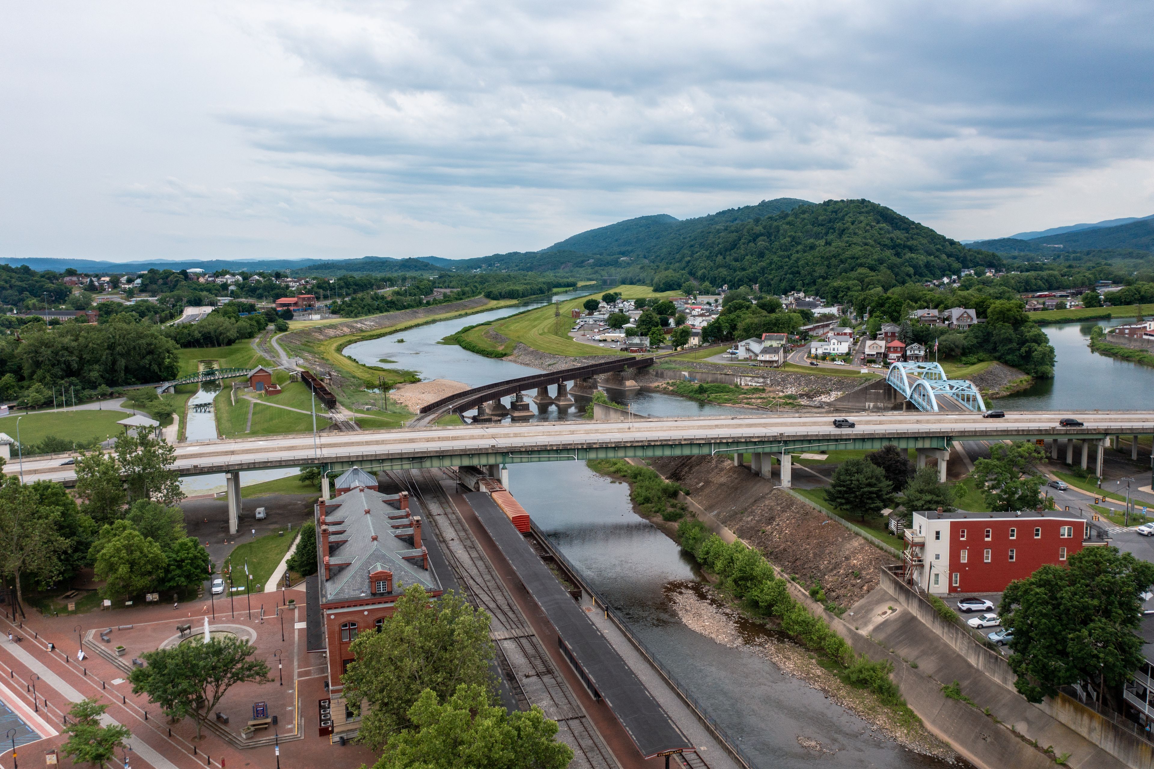 A river with a bridge, a train track, and a town with buildings and greenery.