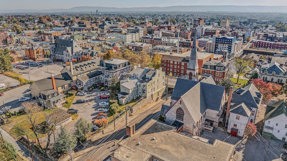 An aerial view of a city with historic buildings, a prominent church steeple, and a distant mountain range.