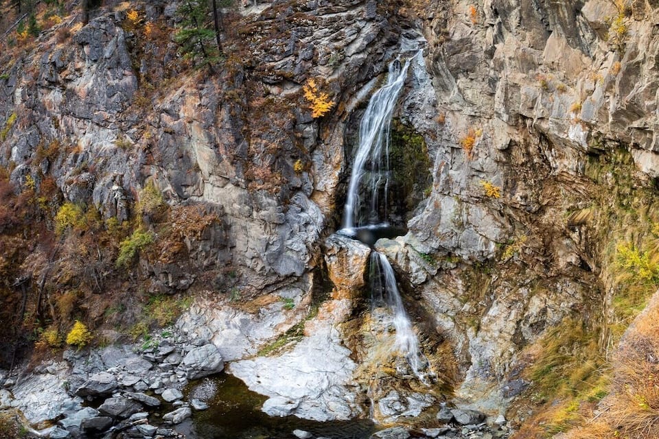 Una cascata che si getta da una scogliera rocciosa, circondata da un foliage autunnale.