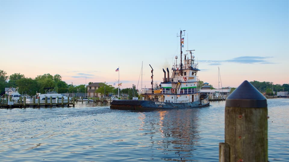 A tugboat named SCHUYLLKILL at a dock with a calm river and a sunset in the background.