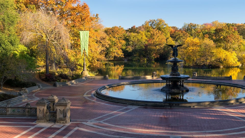 A park with a central fountain, surrounded by a brick pathway and trees with autumn foliage.