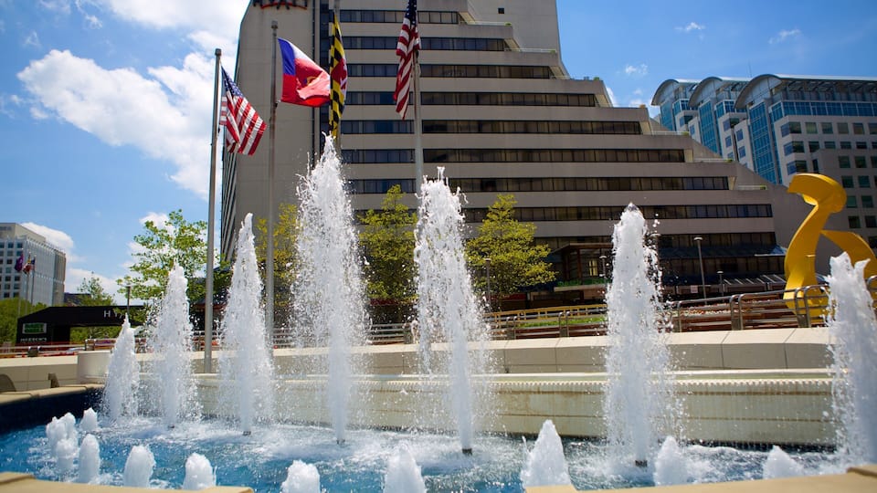 A fountain with multiple jets of water in front of a modern building with flags.