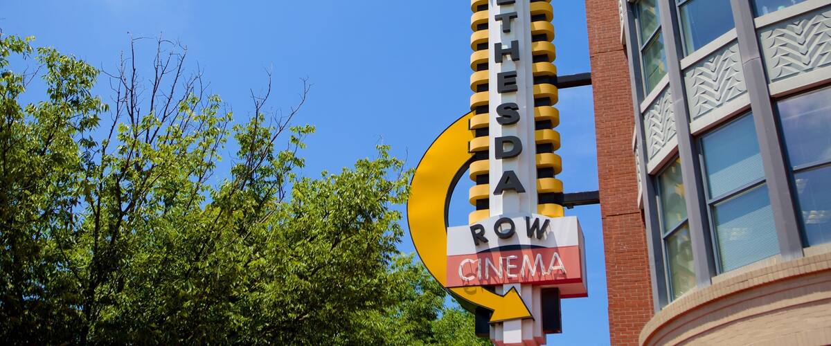 Un cartel de cine con diseño amarillo y blanco, montado en un edificio de fachada de ladrillo y ventanas decorativas.