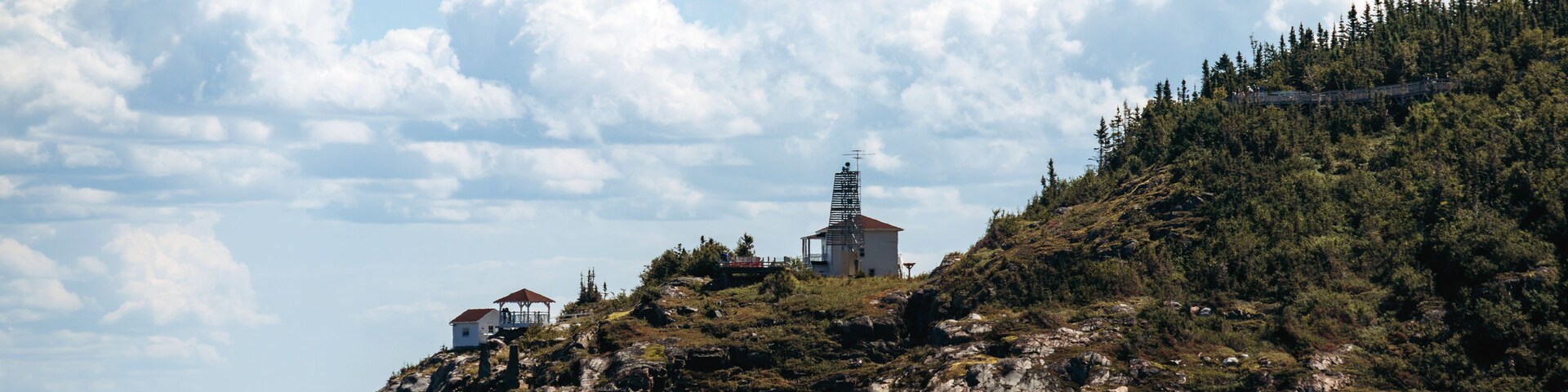 Un paisaje costero con un promontorio rocoso, un faro y una colina boscosa.