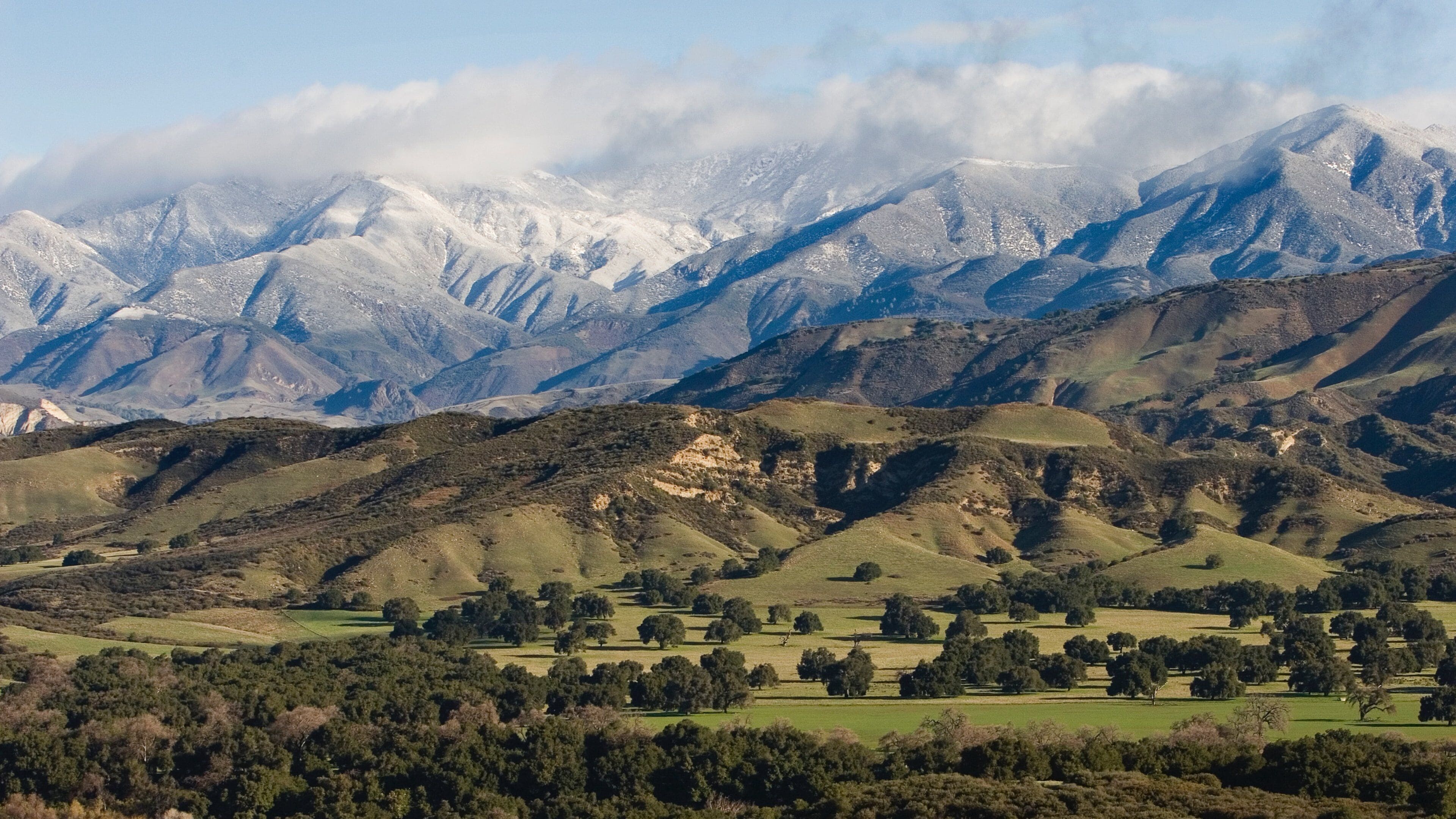 A mountainous landscape with snow-capped peaks and a valley with scattered trees.