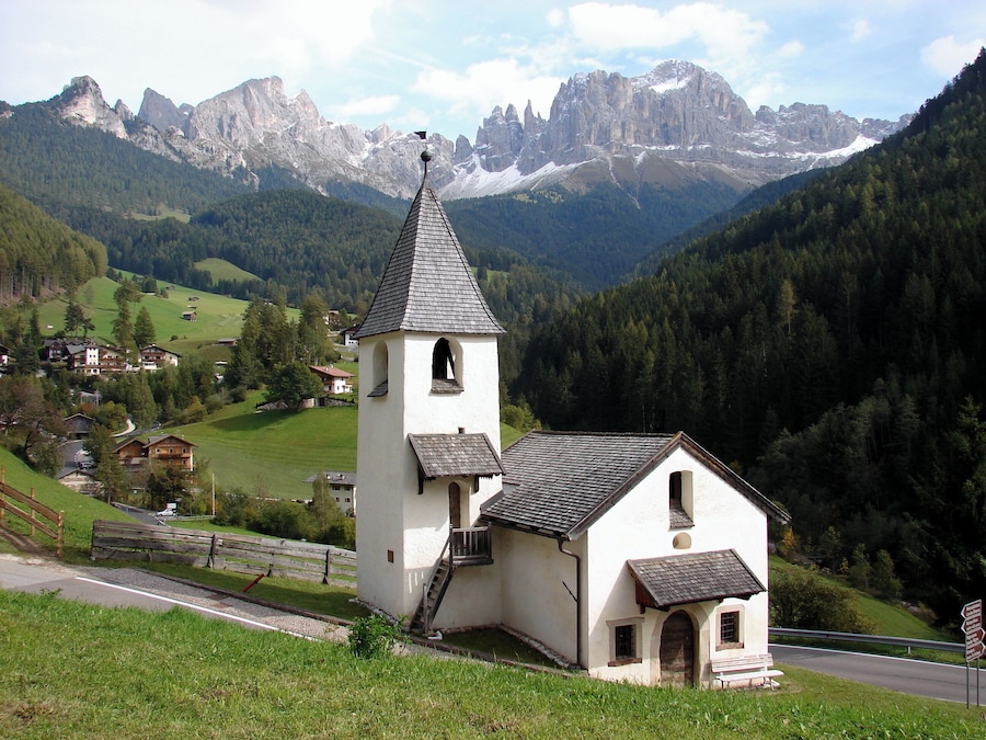 Una iglesia blanca con un campanario y un edificio más pequeño en un valle rodeado de montañas.