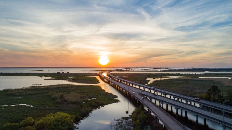 A sunset over a coastal highway with a bridge crossing a river.