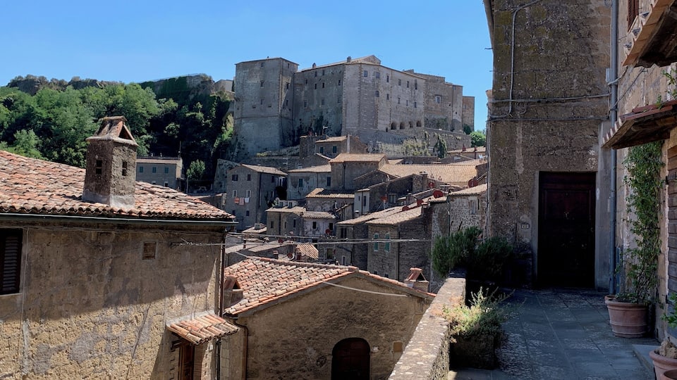 A historic town with stone buildings, a narrow alley, and a prominent castle in the background.