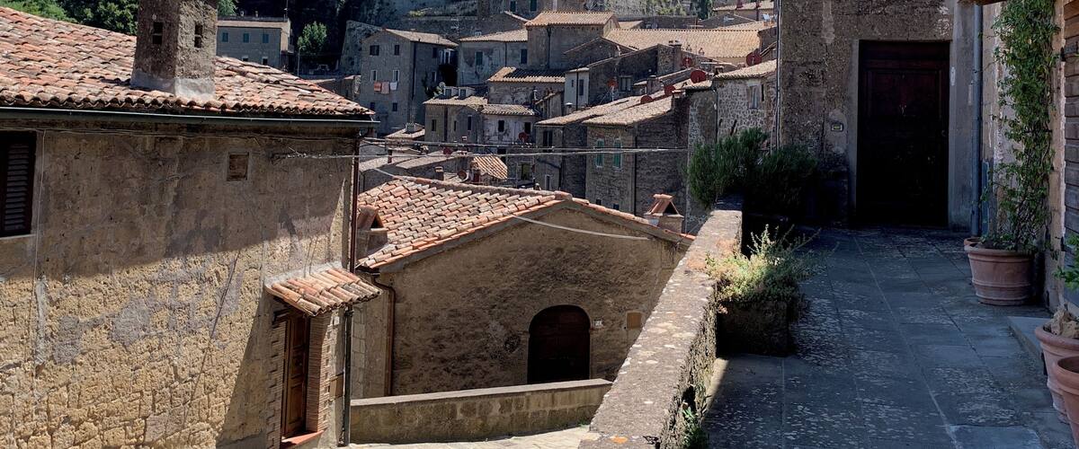 A historic town with stone buildings, a narrow alley, and a prominent castle in the background.