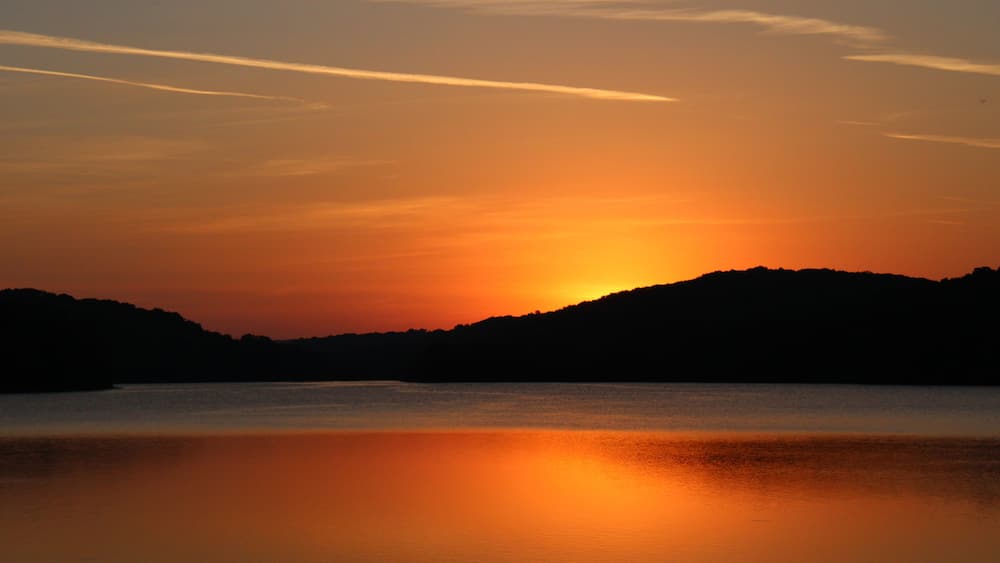 A sunset over a calm body of water with silhouetted hills in the background.
