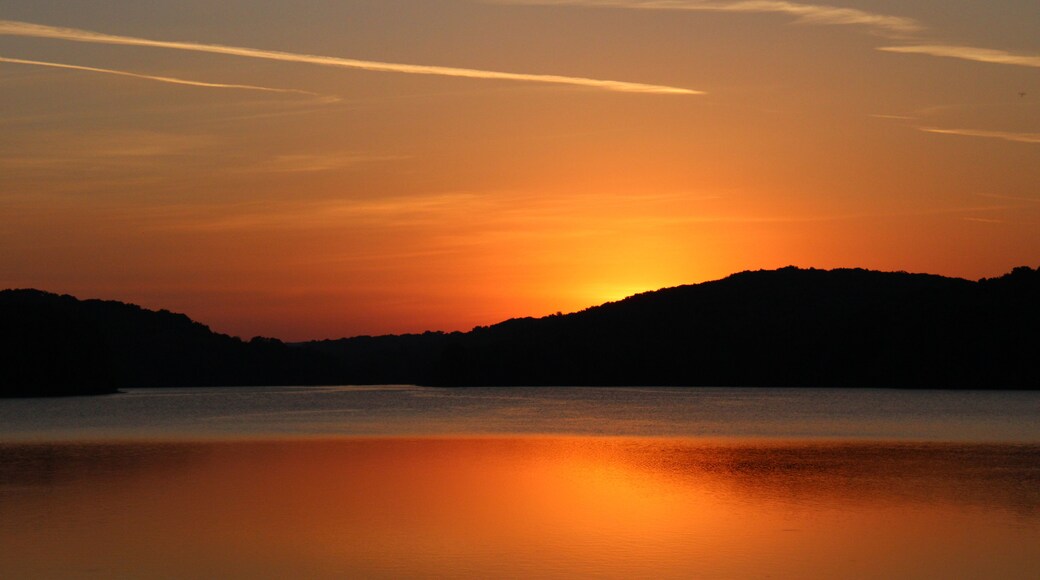 A sunset over a calm body of water with silhouetted hills in the background.