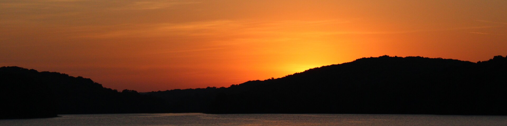 A sunset over a calm body of water with silhouetted hills in the background.
