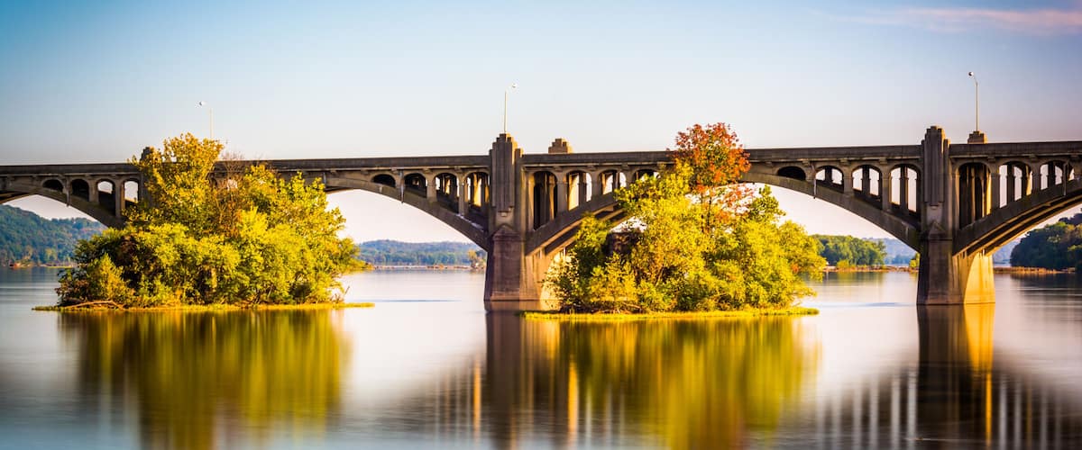 A stone bridge over a calm river with trees reflecting on the water.