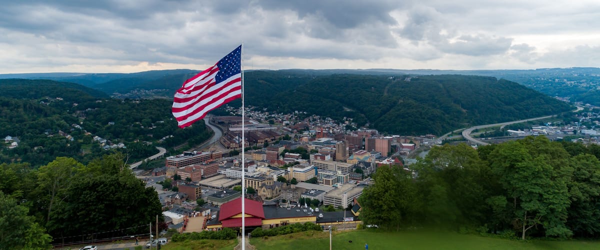 An American flag on a flagpole with a cityscape in the background.