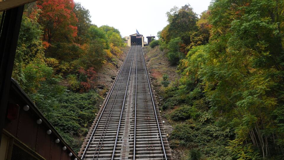 A railway track ascending through a forested area with autumn-colored trees.
