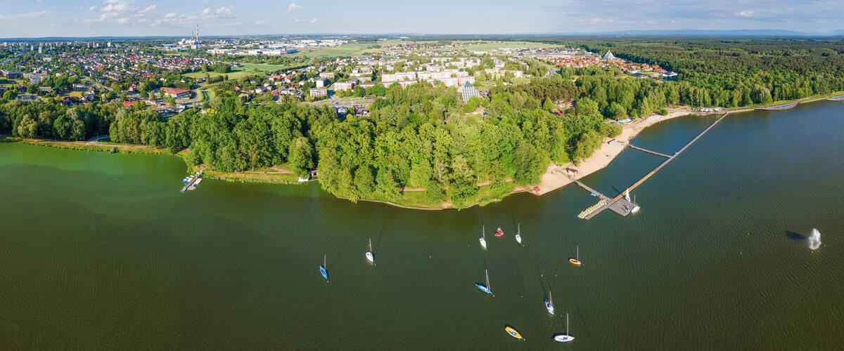 An aerial view of a lakeside town with a bridge, boats, and dense forests.