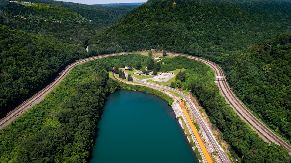 A winding road alongside a river, surrounded by dense forest and hills.