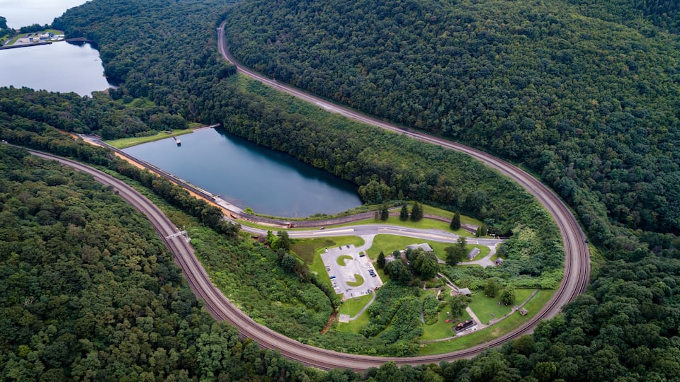 A winding road through a forested area with a lake and a parking lot.