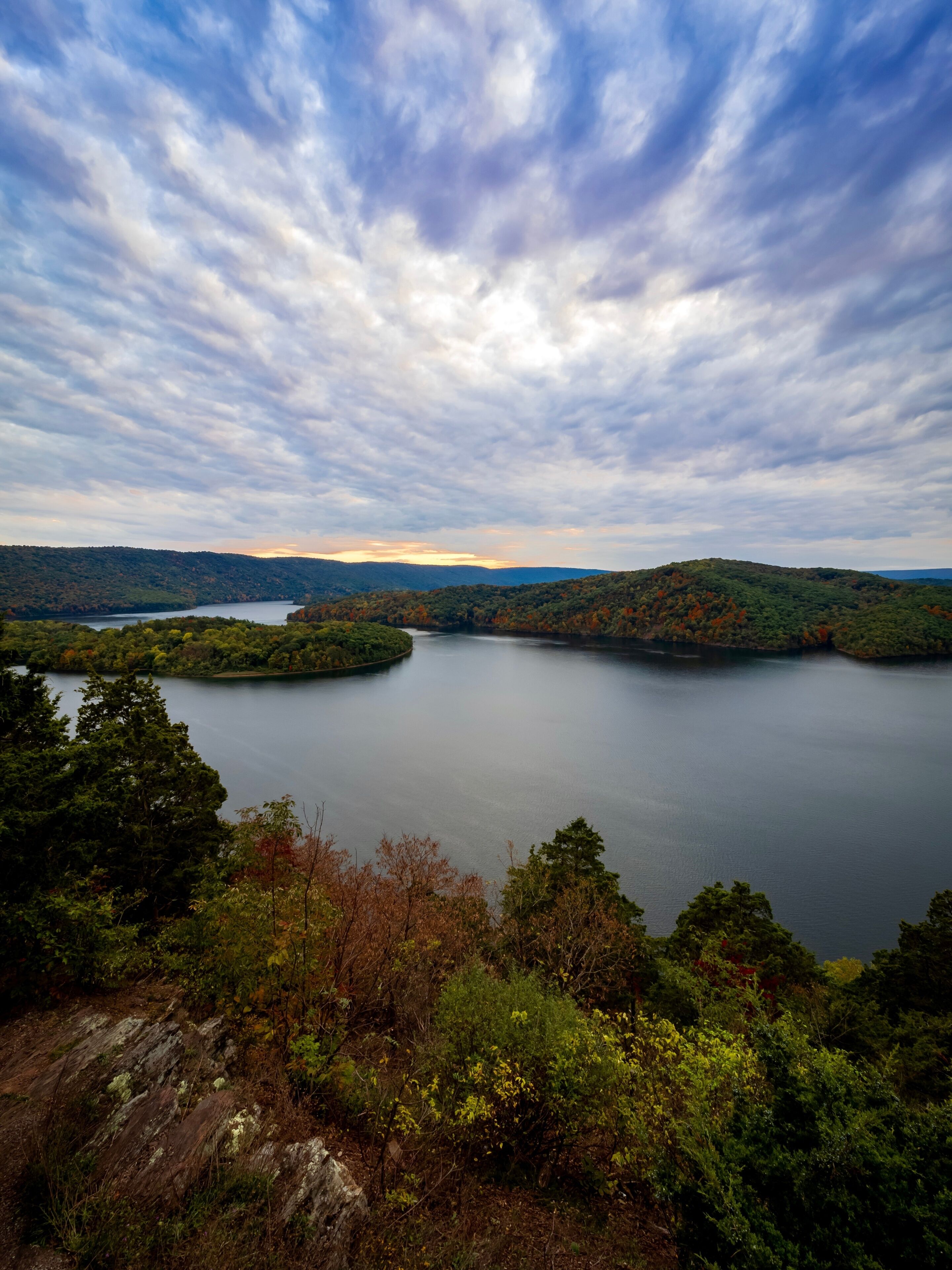 Gorgeous view of Raystown Lake from Hawn’s Overlook near Altoona, Pennsylvania in the fall right before sunset with a view of the dramatic blue sky filled with clouds and pops of pink with foliage.
