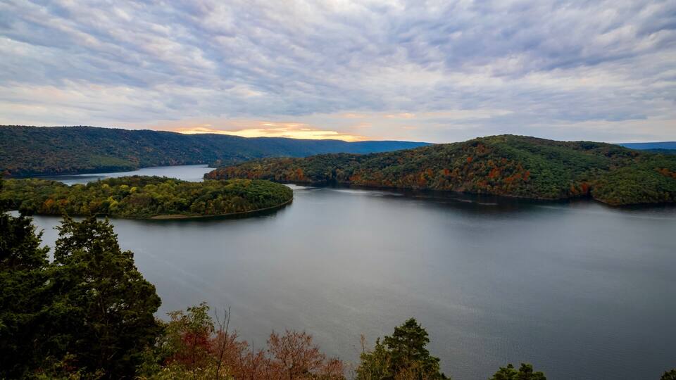 A lake surrounded by forested hills under a cloudy sky.