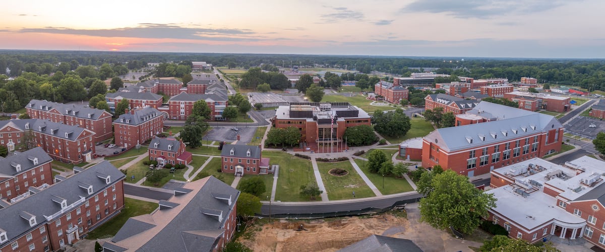 A campus with red brick buildings, green lawns, and a large open field.