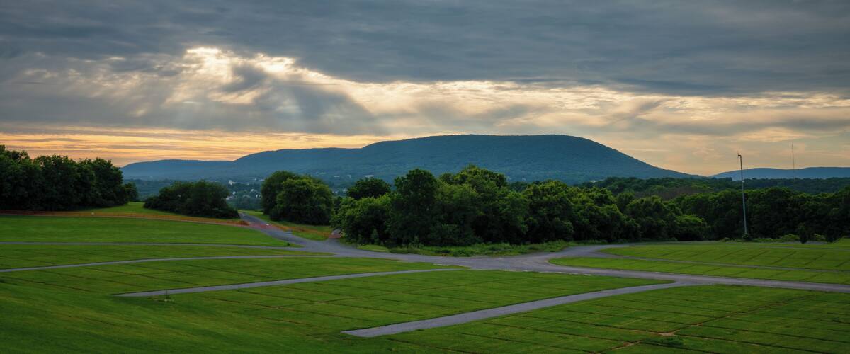 A green field with a winding road, a hill in the background, and a cloudy sky.