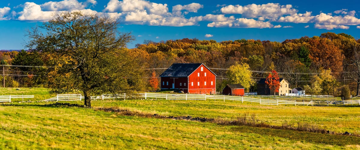 A red barn, white fences, and autumn trees in a rural landscape.