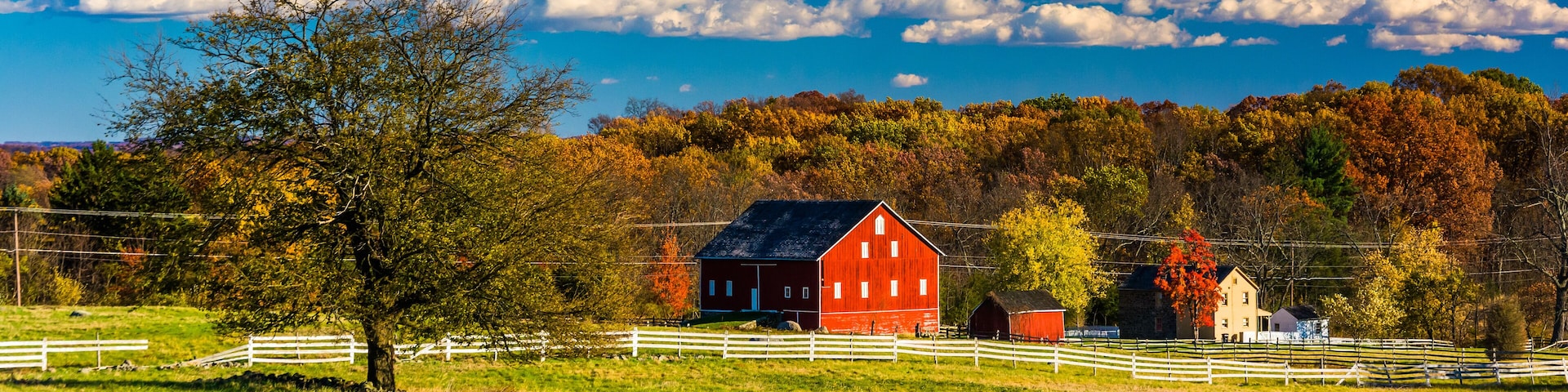 A red barn, white fences, and autumn trees in a rural landscape.